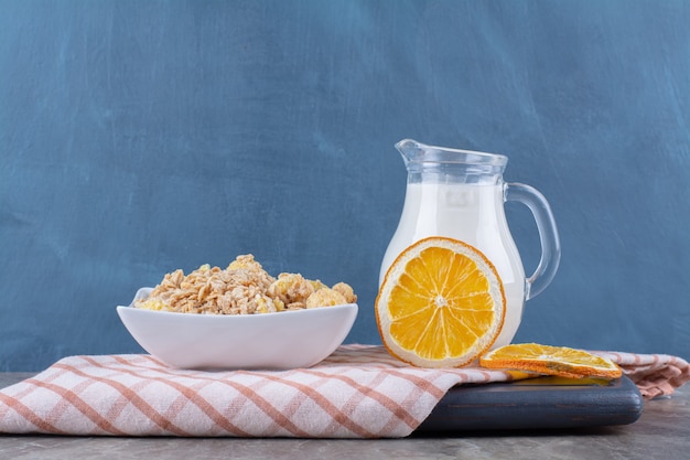 Ein glas milch mit gesunden cornflakes und orangenscheiben auf einem holzbrett.