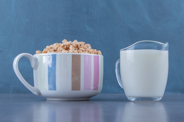 Ein Glas Milch neben Cornflakes in einer Tasse auf dem Marmorhintergrund.