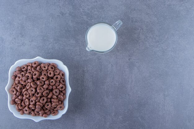 Ein Glas Milch neben Maisringen in einer Schüssel auf dem Marmorhintergrund. Foto in hoher Qualität