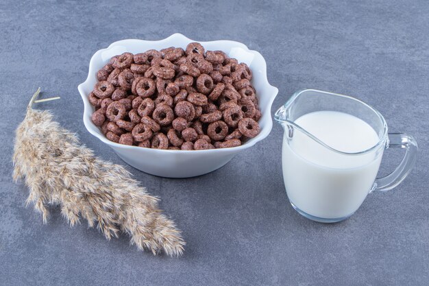 Ein Glas Milch neben Maisringen in einer Schüssel auf dem Marmortisch.