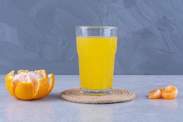 Ein Glas Orangensaft auf einem Untersetzer neben geschnittener Mandarine auf Marmortisch.