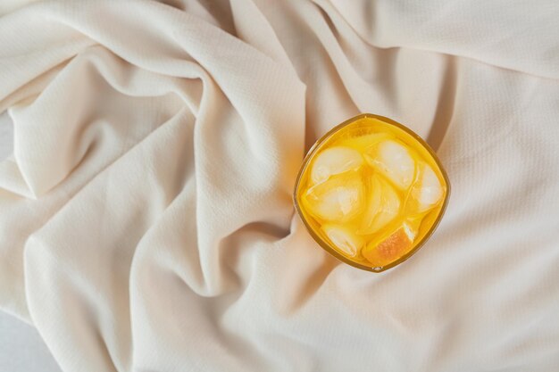 Ein Glas Orangensaft mit Eiswürfeln auf Satinstoff