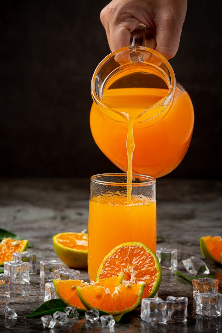 Kostenlose Foto ein glas orangensaft und frisches obst auf dem boden mit eiswürfeln.