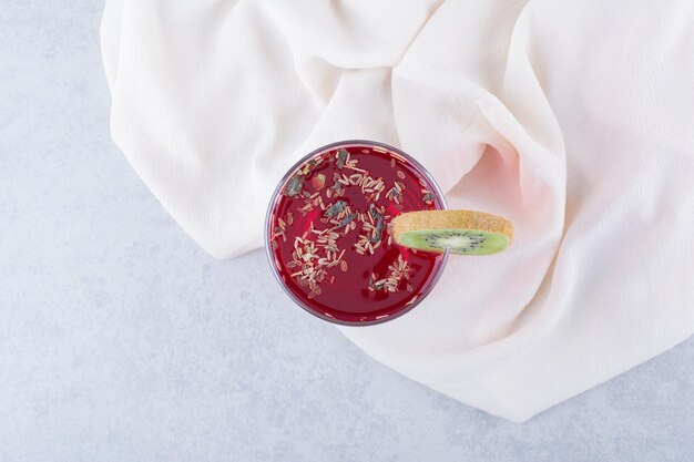 Ein Glas roter Saft auf Tischdecke mit Kiwischeibe.