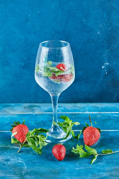 Ein Glas Saft mit Erdbeeren und Minze auf blauer Oberfläche