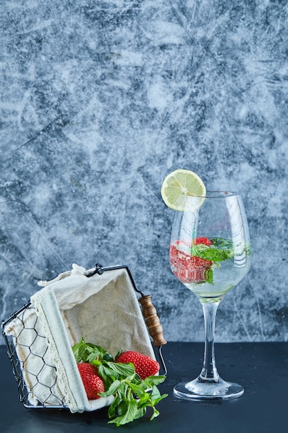 Ein glas saft mit ganzen früchten und einem korb mit erdbeeren auf blauer oberfläche