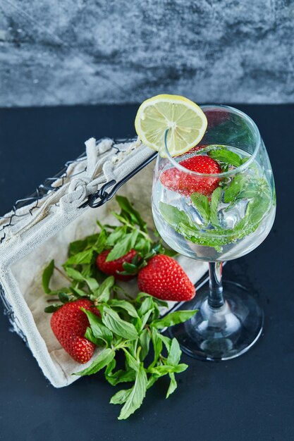 Ein Glas Saft mit ganzen Früchten und einem Korb mit Erdbeeren auf blauer Oberfläche