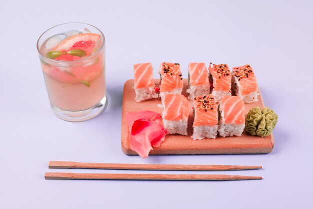 Ein Glas Saft mit klassischen Lachssushi; Wasabi und eingelegter Ingwer auf Schneidebrett mit Essstäbchen vor weißem Hintergrund