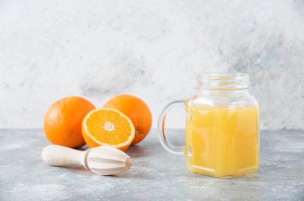 Ein Glaskrug Saft mit frischen Orangenfrüchten auf Steintisch.