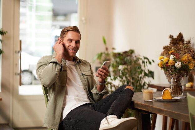 Ein glücklicher, hübscher Mann im Café hört Musik in drahtlosen Kopfhörern und verbindet sich mit dem Café-WiFi.