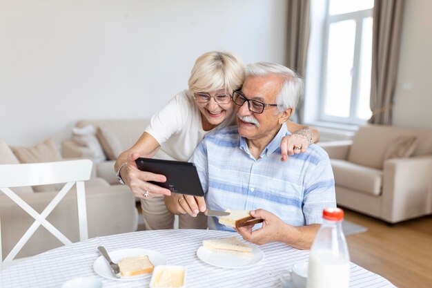 Ein glückliches altes Familienpaar, das mit Enkelkindern spricht, die ein Tablet verwenden, überraschte eine aufgeregte Seniorin, die das Tablet winkte und lächelte