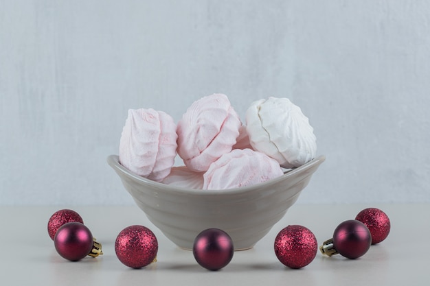 Ein grauer teller mit vanille und rosa zephyren mit weihnachtskugeln.