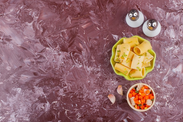 Ein grüner Teller mit trockenen rohen Nudeln mit frisch gemischtem Gemüsesalat und Gewürzen.