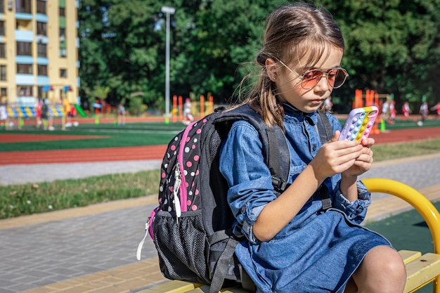 Ein Grundschüler mit Rucksack benutzt ein Smartphone und sitzt in der Nähe der Schule.