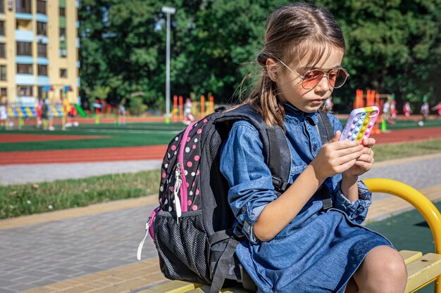 Ein Grundschüler mit Rucksack benutzt ein Smartphone und sitzt in der Nähe der Schule.