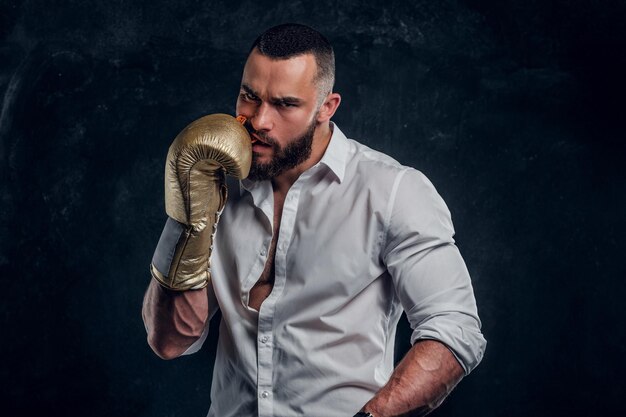 Ein gutaussehender brutaler Mann in schützenden Boxhandschuhen veringt den Mundschutz, während er für den Fotografen posiert.