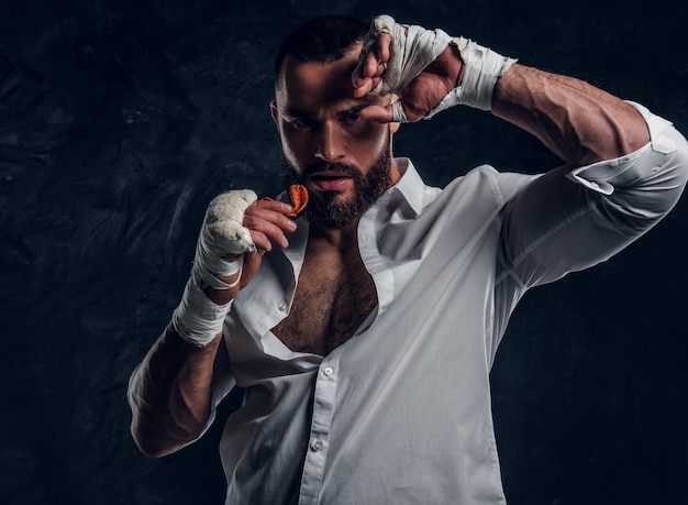 Ein gutaussehender brutaler Mann in schützenden Boxhandschuhen veringt den Mundschutz, während er für den Fotografen posiert.