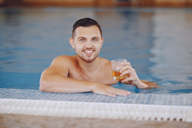 Ein gutaussehender Mann, der zu Hause in ein großes Pool schwimmt und Whisky trinkt