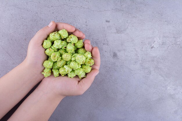 Ein Haufen von aromatisiertem Popcorn, der von zwei Händen auf Marmorhintergrund gehalten wird. Foto in hoher Qualität