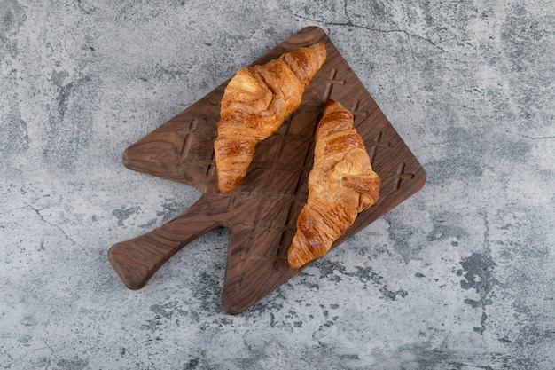 Ein hölzernes Schneidebrett mit frischen Croissants auf einem Steintisch.