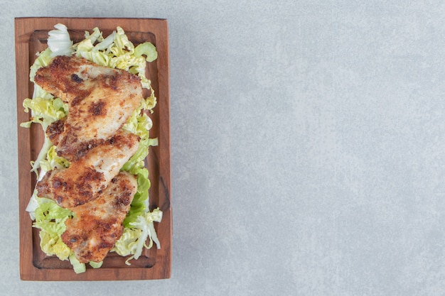 Ein Holzbrett aus gebratenem Hühnerfleisch mit Salat.