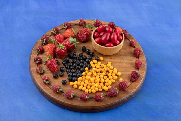 Ein Holzbrett voller Beeren auf blauer Oberfläche