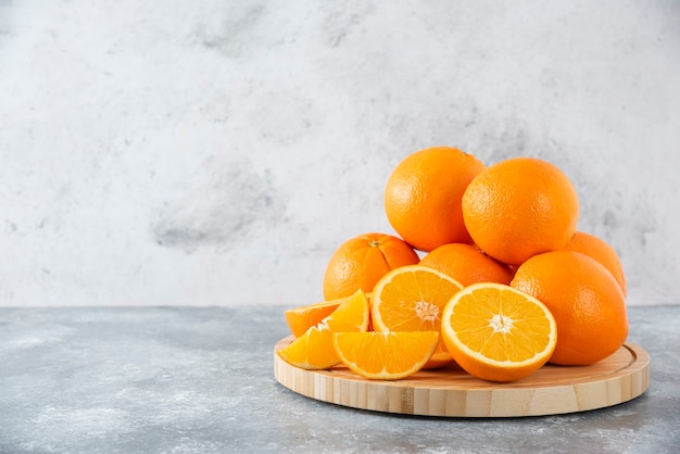 Ein Holzbrett voller saftiger Orangenfruchtscheiben auf Steintisch.