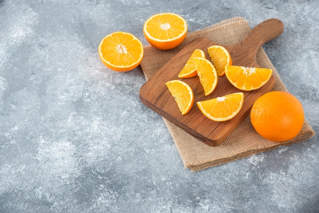 Ein Holzbrett voller saftiger Orangenfruchtscheiben auf Steintisch.