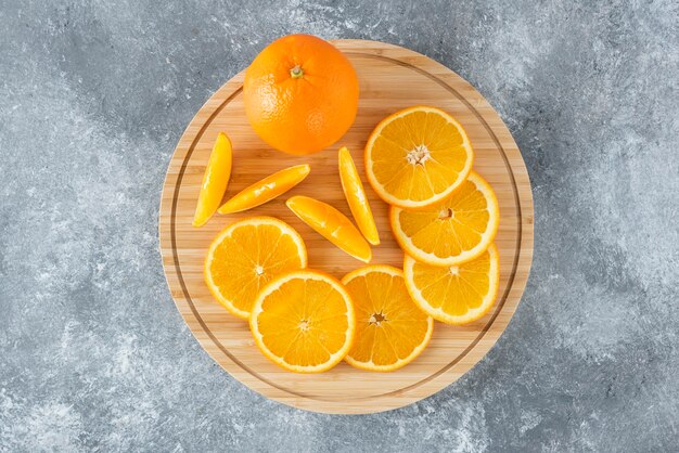 Ein Holzbrett voller saftiger Orangenfruchtscheiben auf Steintisch.