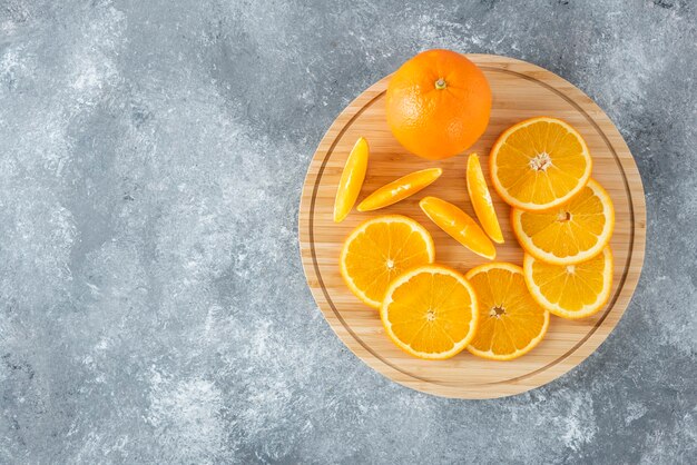 Ein Holzbrett voller saftiger Orangenfruchtscheiben auf Steintisch.