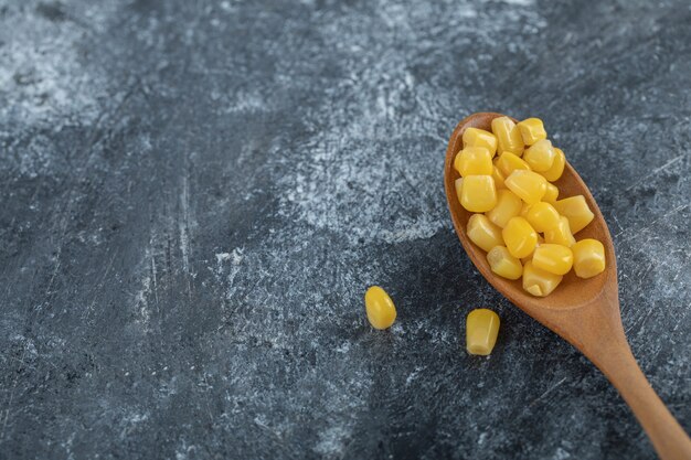 Ein Holzlöffel voller Popcornsamen auf Marmor.