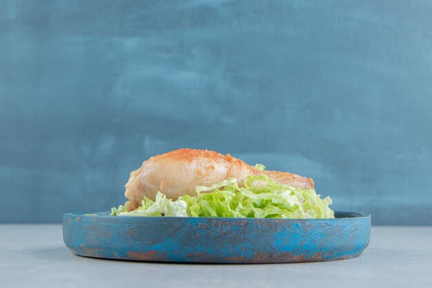 Ein holzteller mit gebratenem hühnerbeinfleisch mit geschnittenem salat.