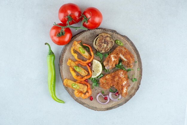 Ein Holzteller mit Paprika und Tomaten auf weißem Tisch.