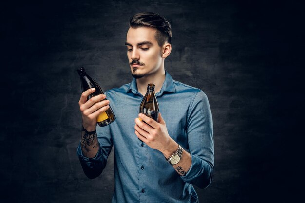 Ein hübscher junger Mann mit einem Tattoo auf seinem Arm hält zwei Craft-Flaschenbiere in der Hand.