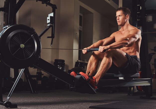 Ein hübscher muskulöser Fitness-Mann, der auf dem Rudergerät trainiert.