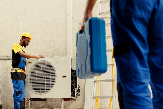 Ein Ingenieur kommt vor Ort an, um dem Lehrling zu helfen, gebrochene elektrische Spulen in beschädigter externer Klimaanlage zu reparieren. Techniker werden beauftragt, innere Teile zu verhindern, um eine rechtzeitige Reparatur zu gewährleisten.