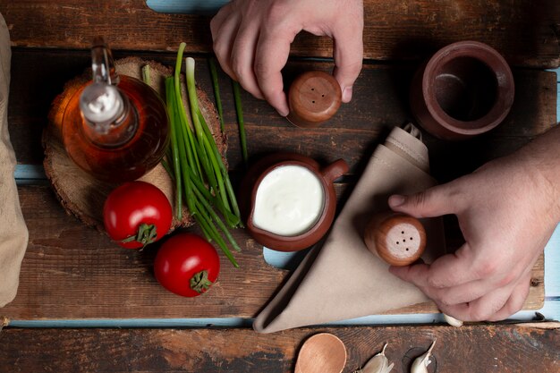 Ein Joghurttopf, Tomaten, Kräuter und eine Olivenflasche auf dem Holztisch