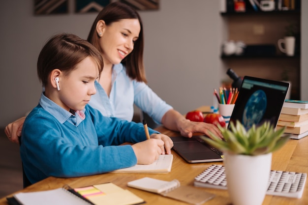 Ein jugendlicher Junge telefoniert mit einem Laptop mit seinem Lehrer neben seiner Mutter über einen Laptop