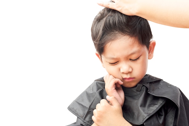 Ein Junge fühlt sich juckend beim Schneiden seines Haares durch den Haaraufbereiter, der über weißem Hintergrund lokalisiert wird