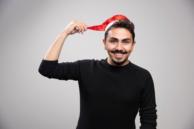 Ein junger brünetter Mann zeigt den Hut seines Weihnachtsmanns und posiert