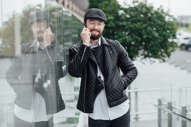 Ein junger, glücklicher, gutaussehender, stilvoller Mann spricht mit dem Mobiltelefon auf den Straßen der Stadt