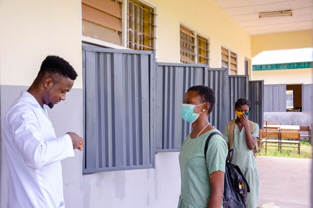 Ein junger gutaussehender afrikanischer klassenlehrer, der als thermometer hält, um die temperatur seines schülers zu scannen, bevor er das klassenzimmer betritt
