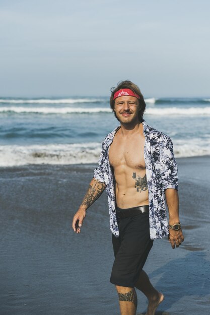 Ein junger gutaussehender Mann in einem roten Bandana geht am Strand entlang.