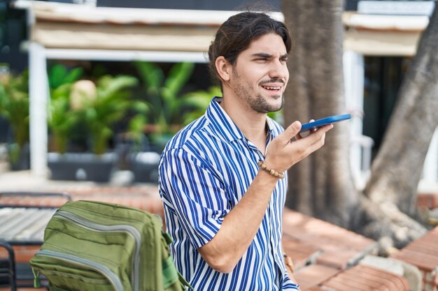 Kostenloses Foto ein junger hispanischer tourist spricht mit seinem smartphone und sitzt auf einer bank im park