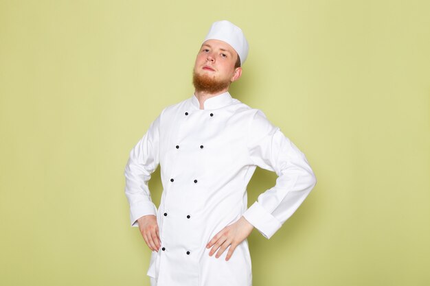 Ein junger männlicher Koch der Vorderansicht in der weißen Kopfkappe des weißen Kochanzugs aufwerfend