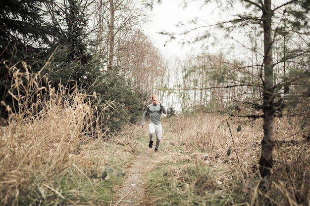 Ein junger Mann, der auf Spur durch Wald läuft