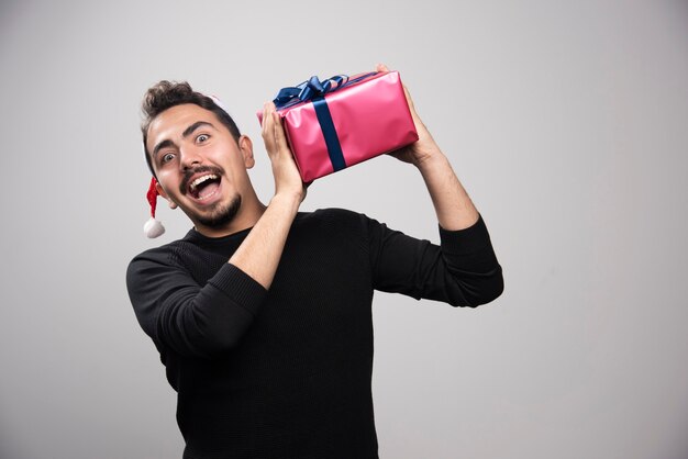 Ein junger Mann, der eine Geschenkbox über einer grauen Wand hält.