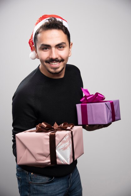 Ein junger Mann, der Geschenkboxen über einer grauen Wand hält.