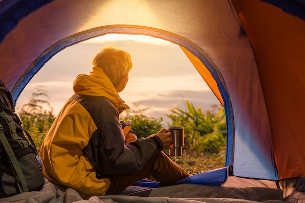 Ein junger Mann, der im Zelt mit dem Halten der Kaffeetasse sitzt