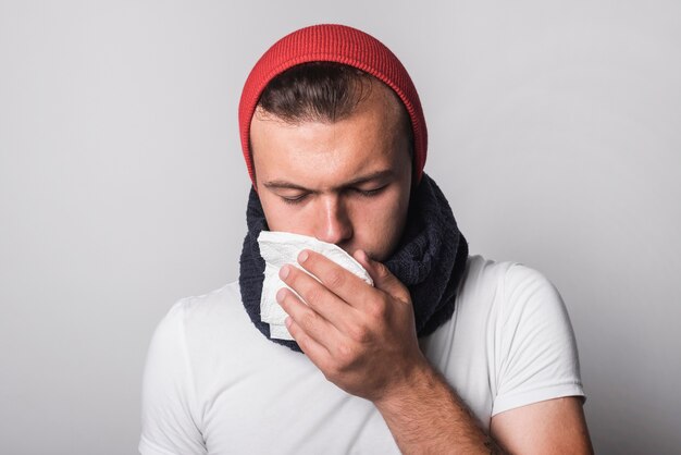 Ein junger Mann, der unter Kälte und Grippe gegen grauen Hintergrund leidet
